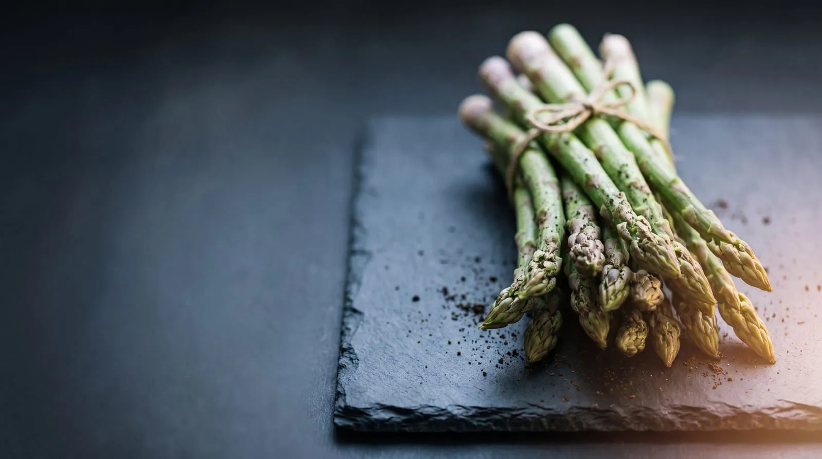 Bos groene asperges met touw samengebonden op een donkere leisteen